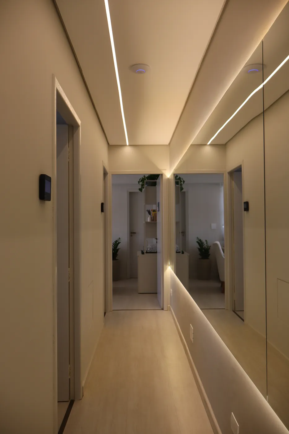 Corredor do espaço com iluminação em LED, parede espelhada e portas das salas
